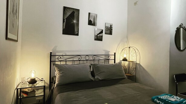 Un dormitorio ordenado con cama, mesitas de noche y luces fijadas a la pared.