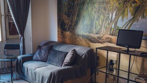 Una sala de estar moderna con un sofá, un televisor sobre un mueble bajo, un cuadro de un paisaje forestal y una mesita con una silla.