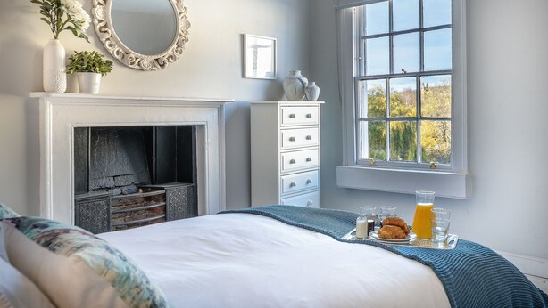 A bedroom with a fireplace, a dresser, a window with a view, and breakfast items on the bed. - The Apartment Bath (Bath)