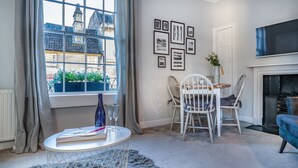 A room with a large window, a fireplace, and a dining area with chairs and a table. - The Apartment Bath (Bath)