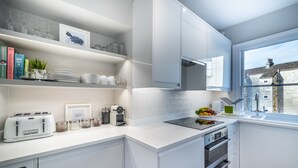 A modern kitchen with white cabinetry, a built-in oven, a sink, and a window with a view of buildings. - The Apartment Bath (Bath)