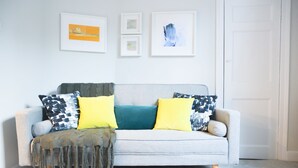 A light grey sofa with yellow and patterned cushions, a grey throw blanket, and three framed artworks on the wall. - The Apartment Bath (Bath)