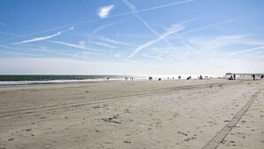 Een breed zandstrand met voetafdrukken en een pier in de verte.
