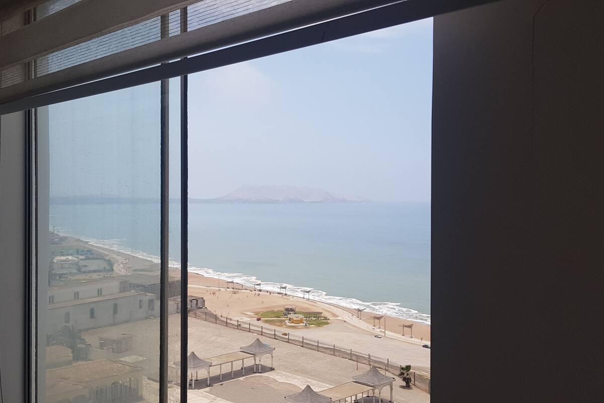 Vista desde una ventana con vista a una playa y cielo despejado.