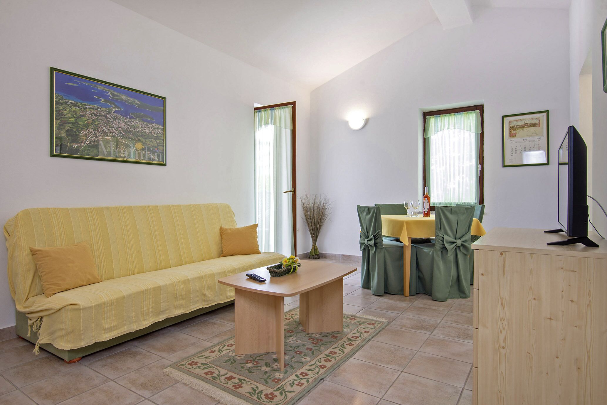 A living room with a sofa, a coffee table, a dining table with chairs, a television, and a painting on the wall.