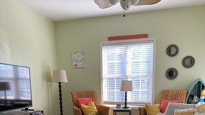 A living room with a television, wicker chairs, a striped sofa, a small table with a lamp, and a window with blinds. - CLOSE TO ALL, a block from BEACH/BOARDS/ FAMILY FUN..Did we mention HEATED POOL! (Wildwood)