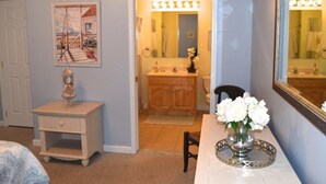 A bedroom with a bed, a nightstand, a dresser, a vanity with a mirror, and a vase of flowers on a table. - CLOSE TO ALL, a block from BEACH/BOARDS/ FAMILY FUN..Did we mention HEATED POOL! (Wildwood)