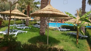 A poolside area with thatched umbrellas, white lounge chairs, and palm trees. - Azur Plaza (Hammamet)