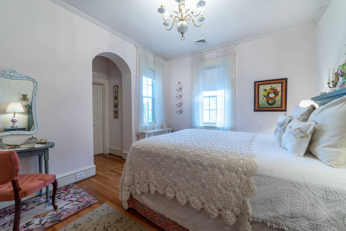 A bedroom with a large bed, a vanity with a mirror, and a chandelier.