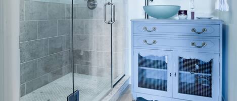 Un baño moderno con cabina de ducha de vidrio, tocador con lavamanos y espejo sobre el tocador.