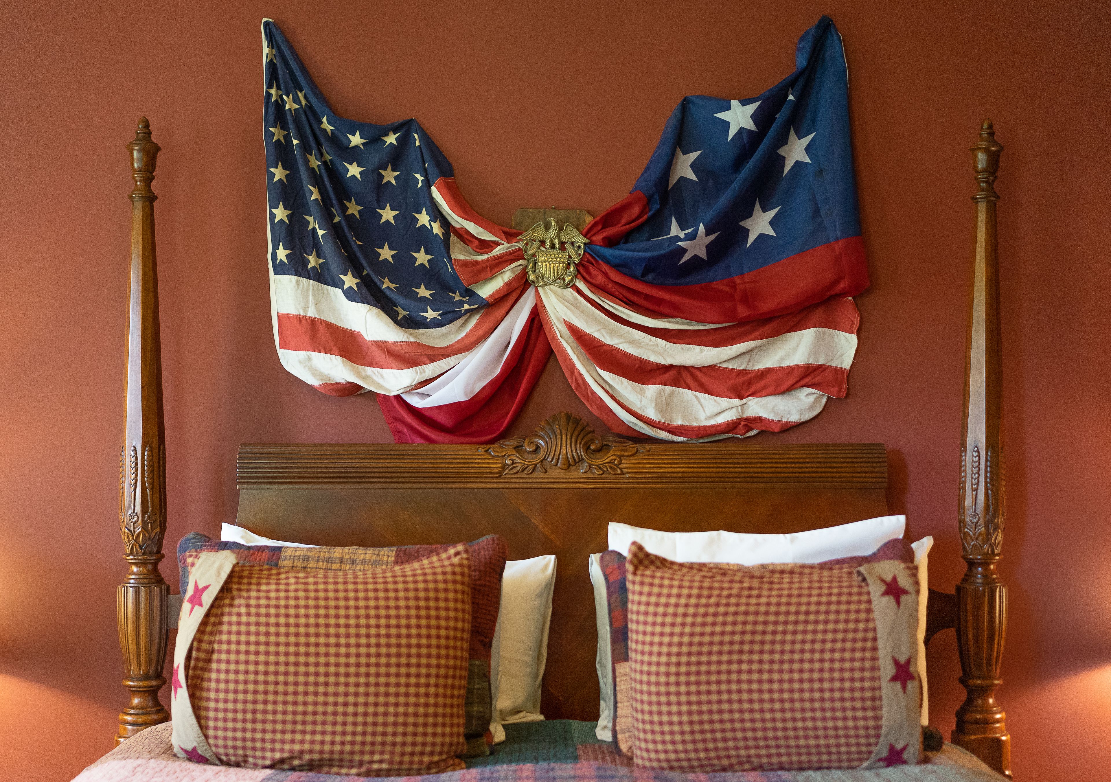 Una cama con cabecera, dos banderas y almohadones a cuadros.
