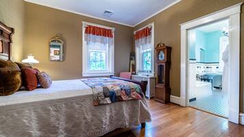 A bedroom with a large bed, a wooden dresser, a clock, and a view of the bathroom through an open door.