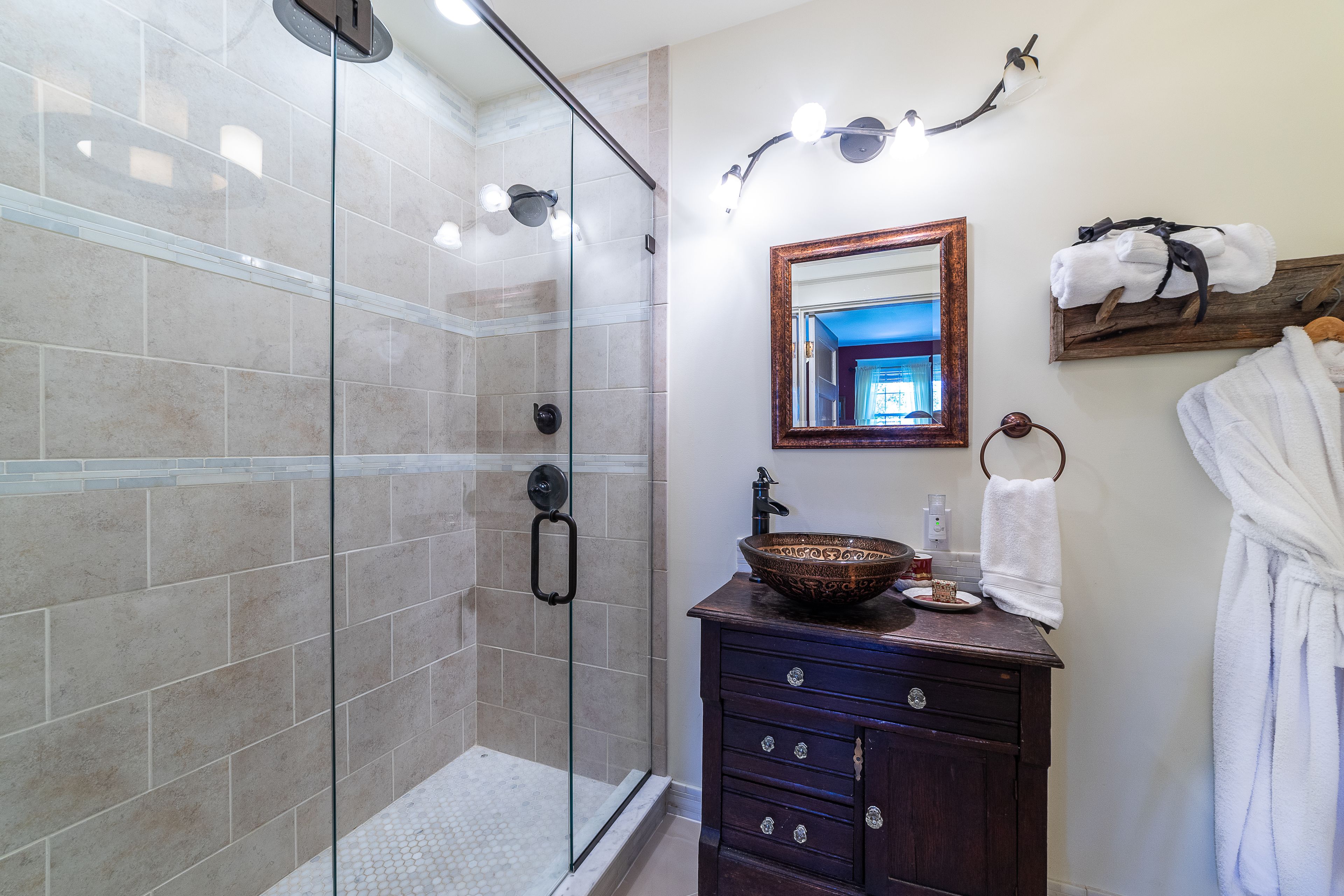 A modern bathroom with a glass-enclosed shower, a wooden vanity with a bowl sink, and a mirror with a wooden frame.