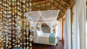 A room with a bed, hanging shells, and a thatched roof. - Calala Island (Laguna de Perlas)