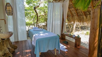 A wooden deck with a bed, a wooden bench, and a small table with bottles.