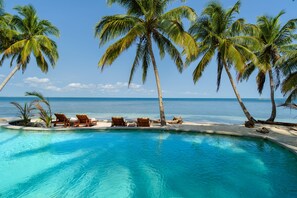 A pool with clear blue water, surrounded by palm trees and a sandy beach.