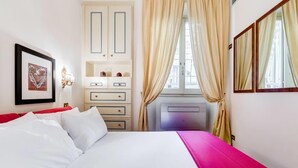 A bedroom with a bed, a dresser, a vanity, and a window with curtains. - Elegant apartment Rome (Roma)