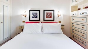 A hotel room with a bed, two framed pictures on the wall, a nightstand, and a dresser with drawers. - Elegant apartment Rome (Roma)
