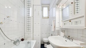 A bathroom with a bathtub, toilet, and sink, featuring white tiles and a small window. - Elegant apartment Rome (Roma)