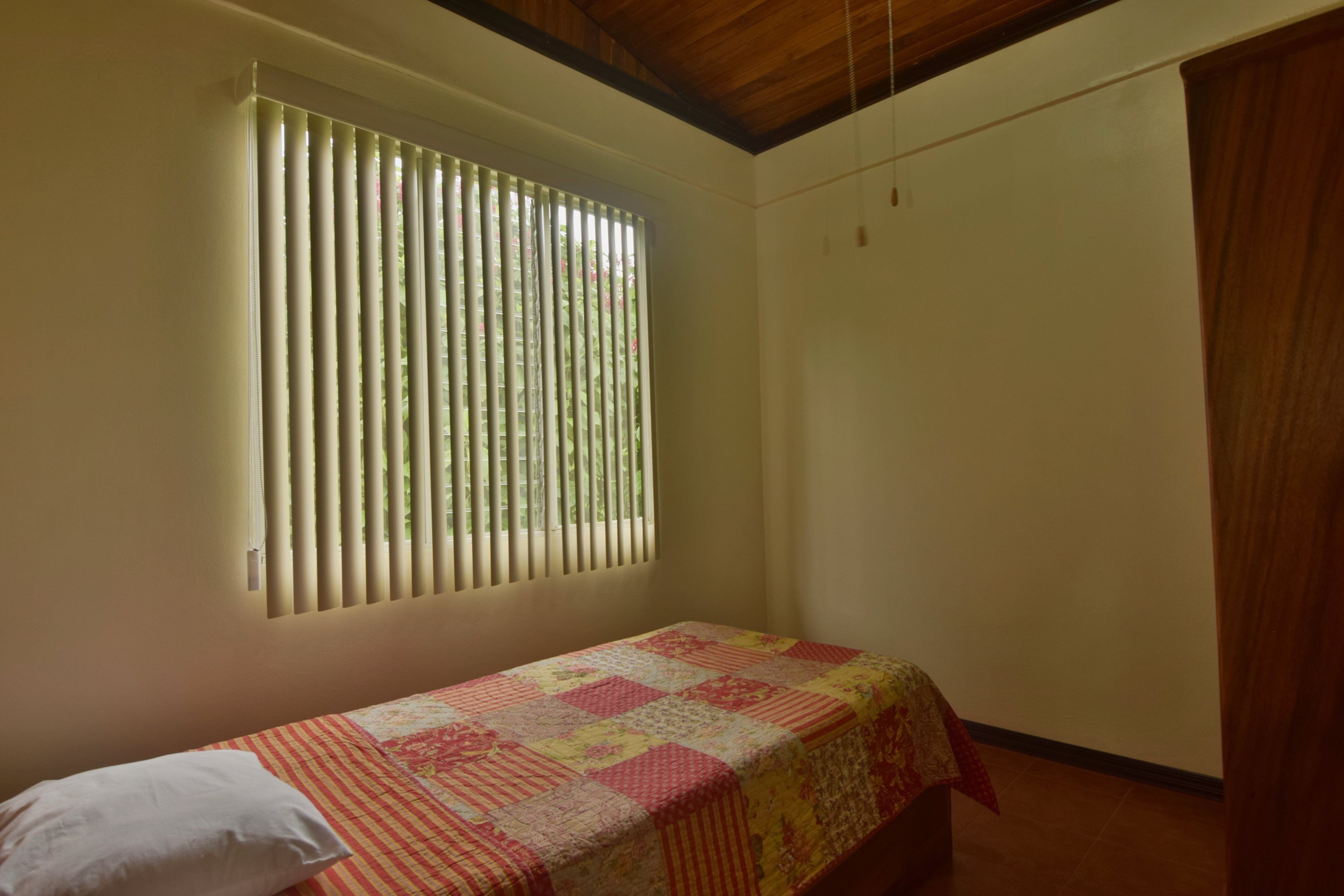 Una habitación pequeña con una cama individual, techo de madera, ventana con persianas y colcha acolchada.