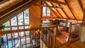 Un loft spacieux avec de hauts plafonds, des poutres apparentes et de grandes fenêtres offrant une vue sur la forêt environnante.