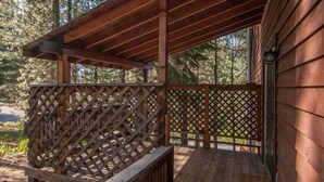 Une terrasse en bois avec une balustrade en treillis, un banc et une vue sur une zone boisée.