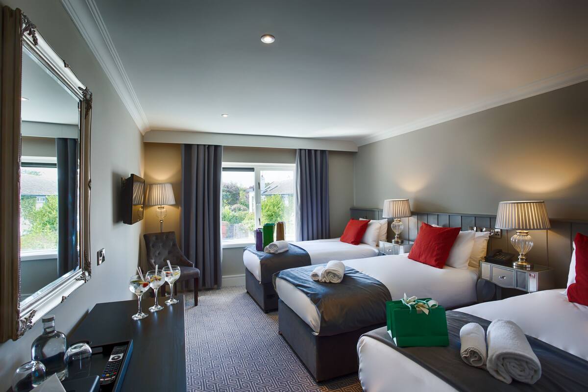 A hotel room with two beds, a desk with a lamp, a mirror, and a window with curtains.