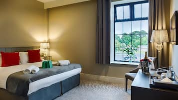 Habitación de hotel con una cama grande, un escritorio, un ventanal con cortinas y vistas al exterior con vegetación.