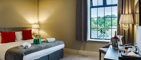 Habitación de hotel con una cama grande, un escritorio, un ventanal con cortinas y vistas al exterior con vegetación.