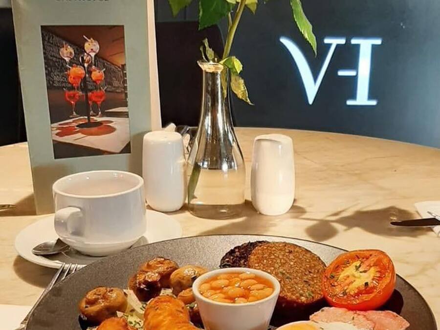 Un plato de desayuno con salchichas, huevos, tocino, frijoles y tomate. Se observa un jarrón con una rosa roja y un menú titulado 'BULL & TIDE GASTROPUB'.