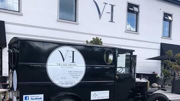 Un camión de reparto negro antiguo estacionado frente a un edificio blanco con las letras