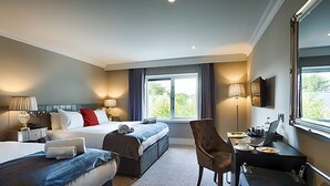 A hotel room with two beds, a desk with a laptop, a chair, and a large window. - Village Hotel (Bettystown)