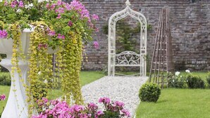 A garden with a white bench, a white archway, and a ladder. - Village Hotel (Bettystown)