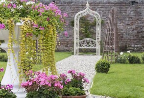 Un jardín con un banco blanco, un arco blanco y una escalera.