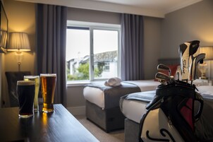 Una habitación de hotel con una cama, un escritorio con vasos de cerveza y un bolso de golf.