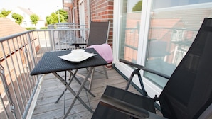 Un balcon avec une table et des chaises, un chapeau blanc sur la table et une serviette rose sur une chaise.
