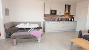 Un espace de vie compact comprenant un coin cuisine, un coin repas avec une table et un banc, et un canapé.