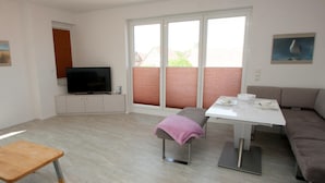 Un salon moderne avec un téléviseur à écran plat, un canapé, une table sur laquelle est posée une serviette rose et un tabouret en bois.