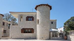 Un bâtiment en pierre doté d’une tour, de fenêtres avec volets et d’une entrée fermée par un portail.
