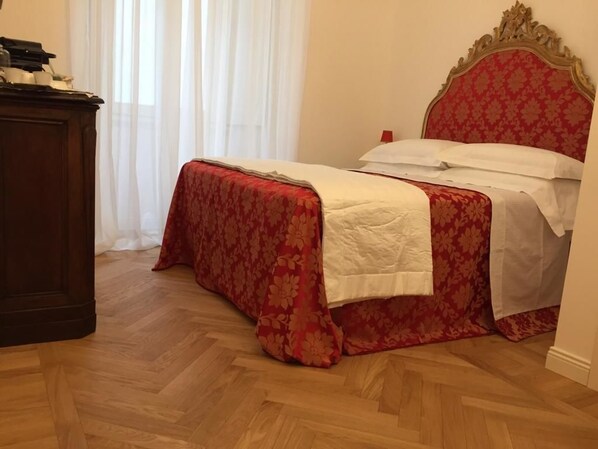 A neatly made bed with a red floral bedspread and white linens, a wooden nightstand with a lamp, and a classic headboard. - La Belle Coquette B&B (Como)