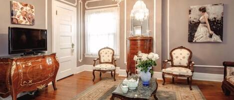 A traditional living room with a television, two armchairs, a coffee table, and a chandelier.