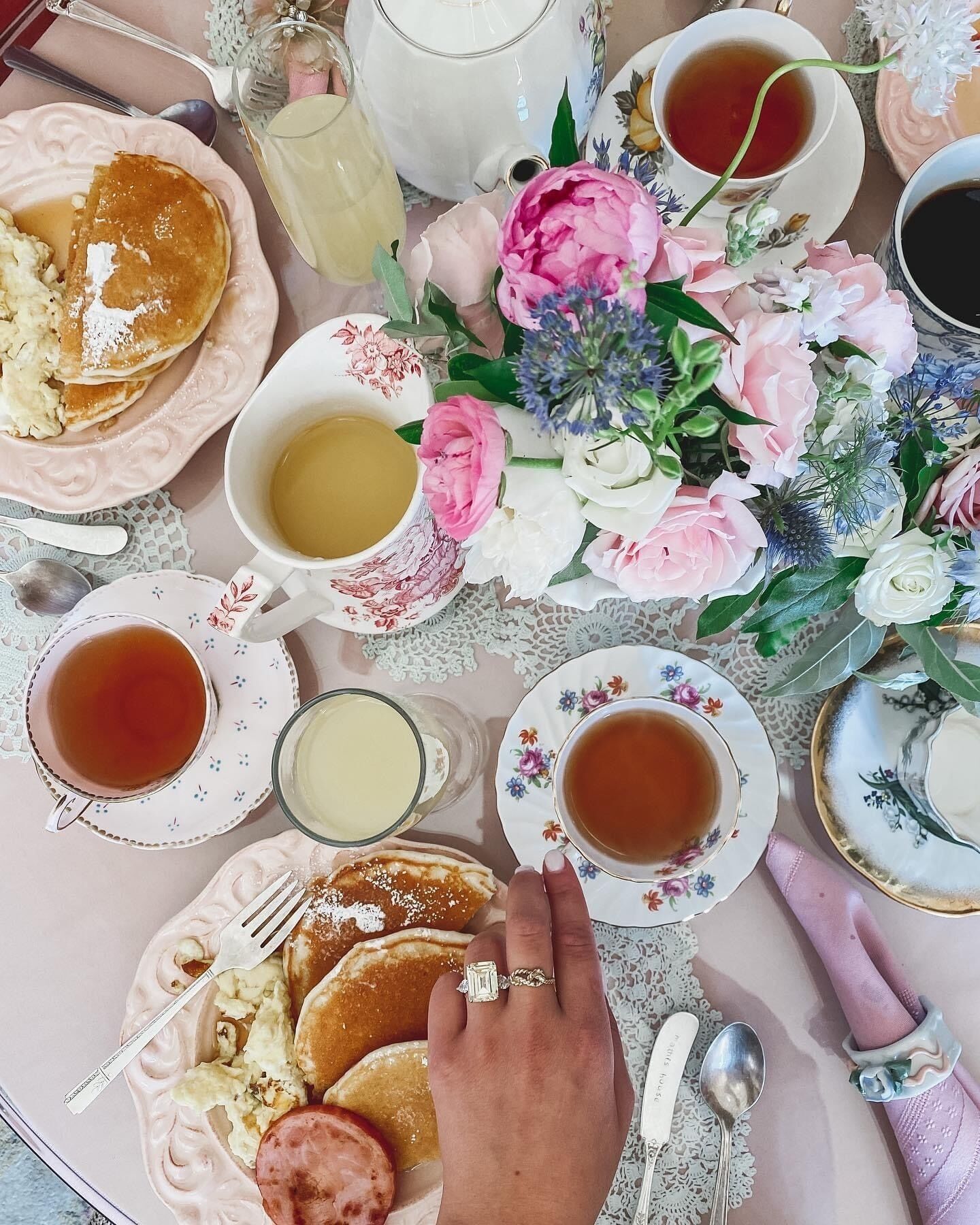 A table set with pancakes, tea, and a floral arrangement.