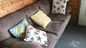 Un canapé marron agrémenté de trois coussins à motifs, dans une pièce dont les murs sont recouverts de lambris en bois et où se trouve un tapis gris.