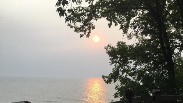 Une table avec une bouteille et une assiette de nourriture, donnant sur une étendue d’eau, avec un coucher de soleil en arrière-plan.