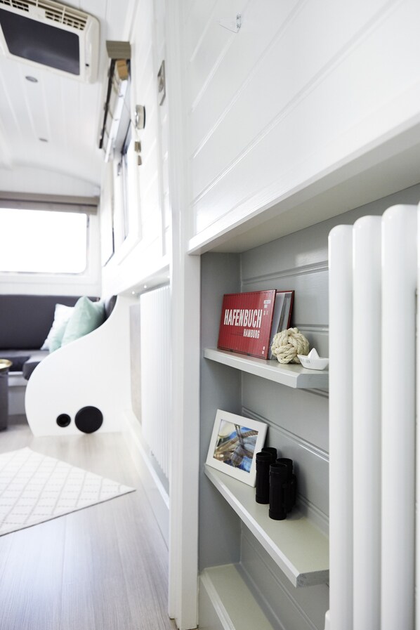 Un interior moderno con un sofá blanco, una estantería con libros y objetos decorativos, y una pared blanca con un radiador.