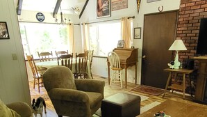 Un salon avec un canapé, un fauteuil et un pouf, un piano, un chien et un téléviseur.
