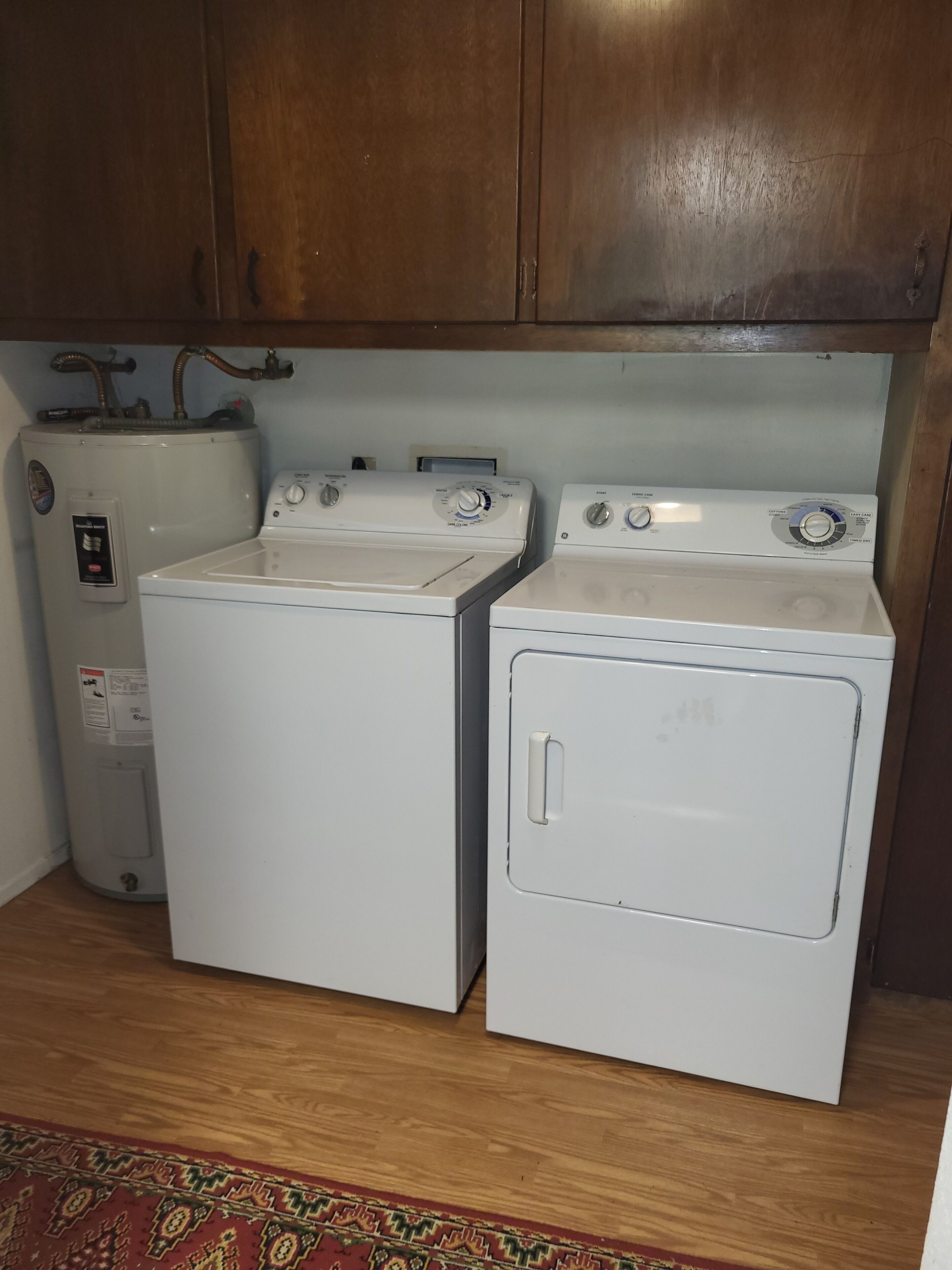 Een wasserette met twee witte wasmachines, een boiler en houten kasten.