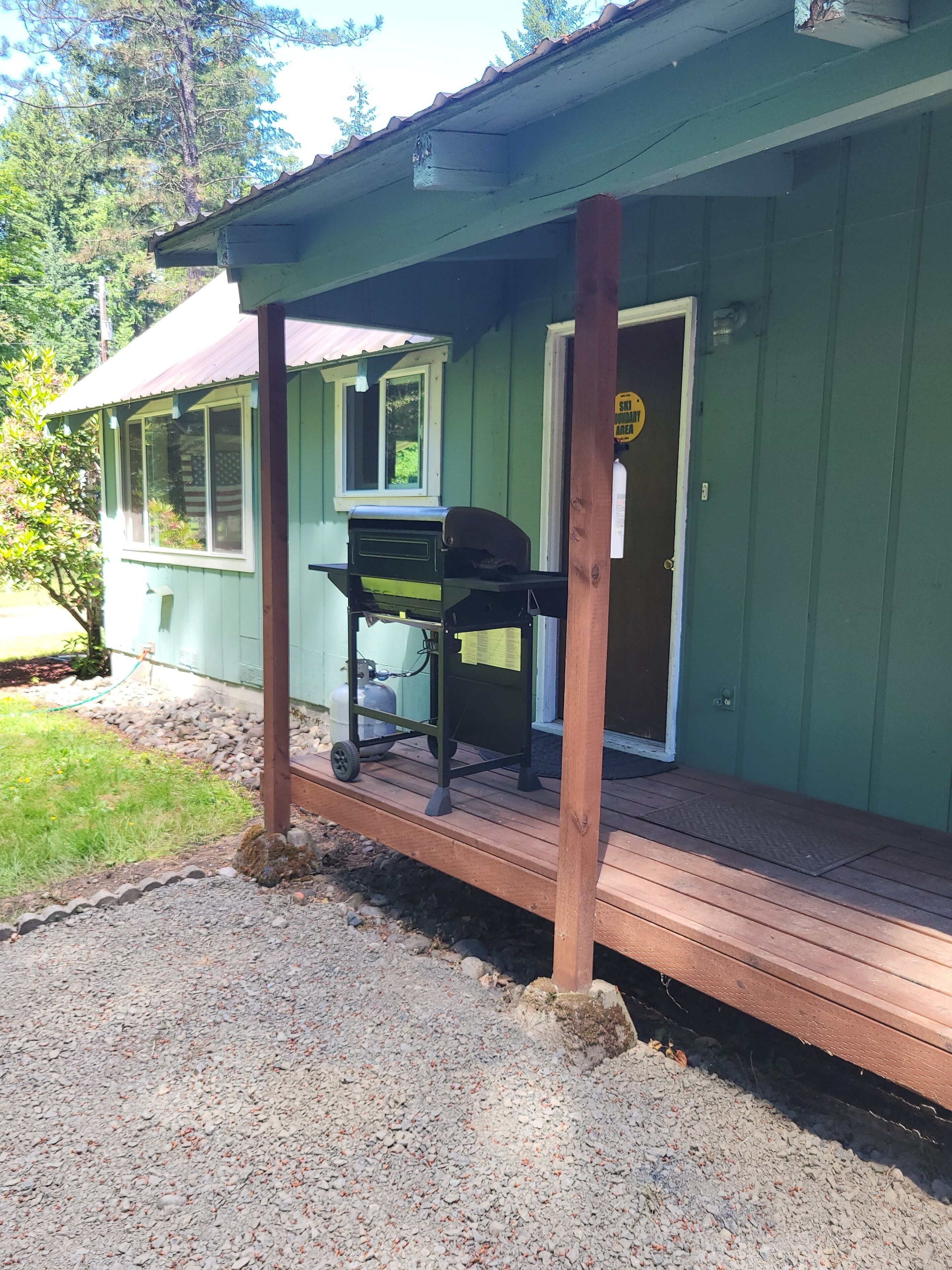 A green house with a wooden deck, a grill, and a propane tank.