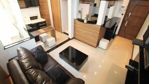 A modern living room with a leather sofa, a glass coffee table, and a kitchen area with a white refrigerator and wooden cabinets. - Apartments Almirante Gonçalves (Rio de Janeiro)