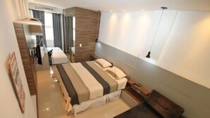 A modern hotel room with a large bed, a small desk, a sofa, and a window with curtains. - Apartments Almirante Gonçalves (Rio de Janeiro)